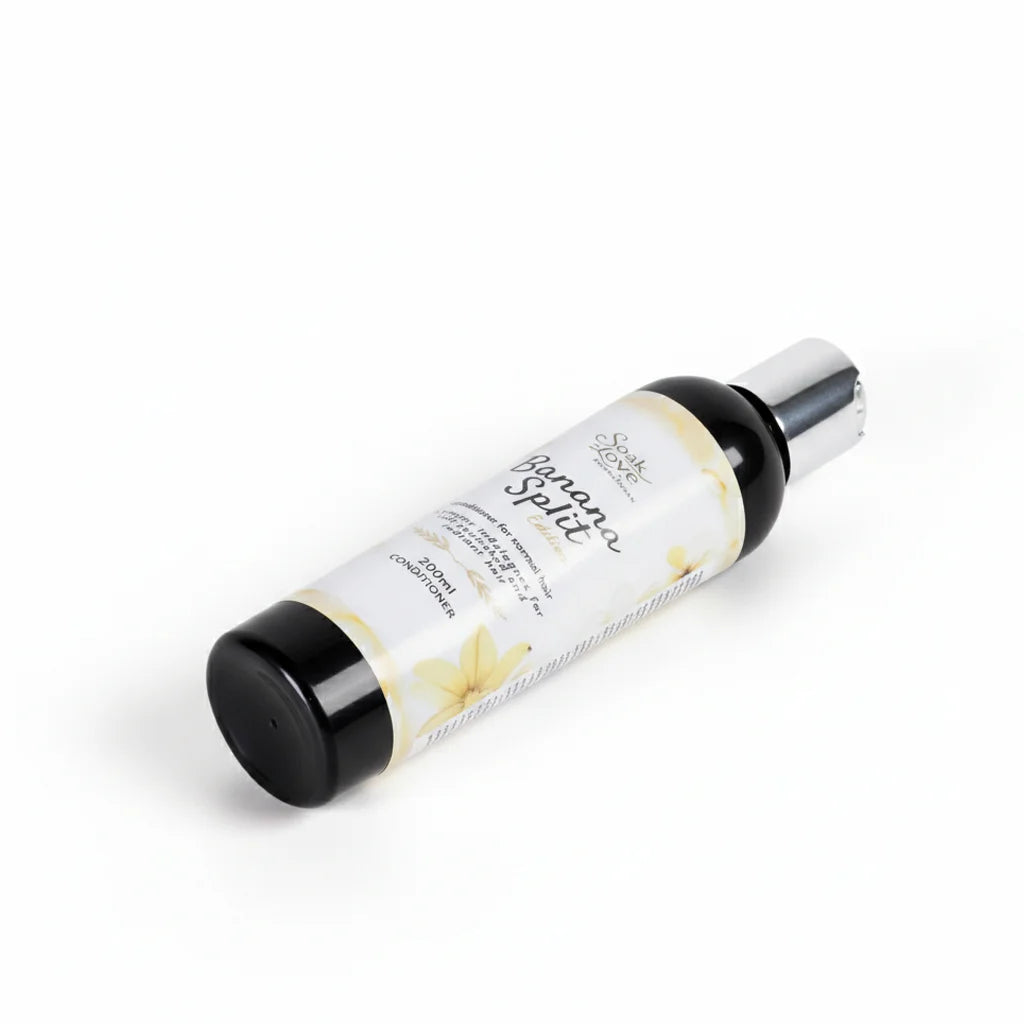 Hand holding a 200ml bottle of Soak in Love Banana Split Edition Conditioner for normal hair with a white and yellow label against a white background.
