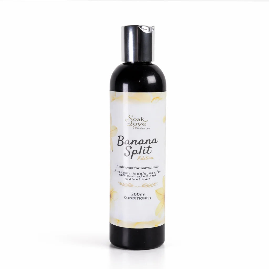 Hand holding a 200ml bottle of Soak in Love Banana Split Edition Conditioner for normal hair with a white and yellow label against a white background.