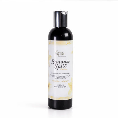 Hand holding a 200ml bottle of Soak in Love Banana Split Edition Conditioner for normal hair with a white and yellow label against a white background.